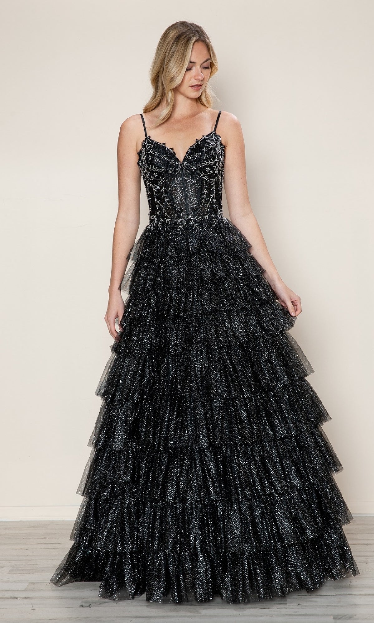 A woman in the Long Prom Dress: Poly USA 9608—black, with a ruffled tiered skirt and beaded lace corset bodice—stands against a plain background.